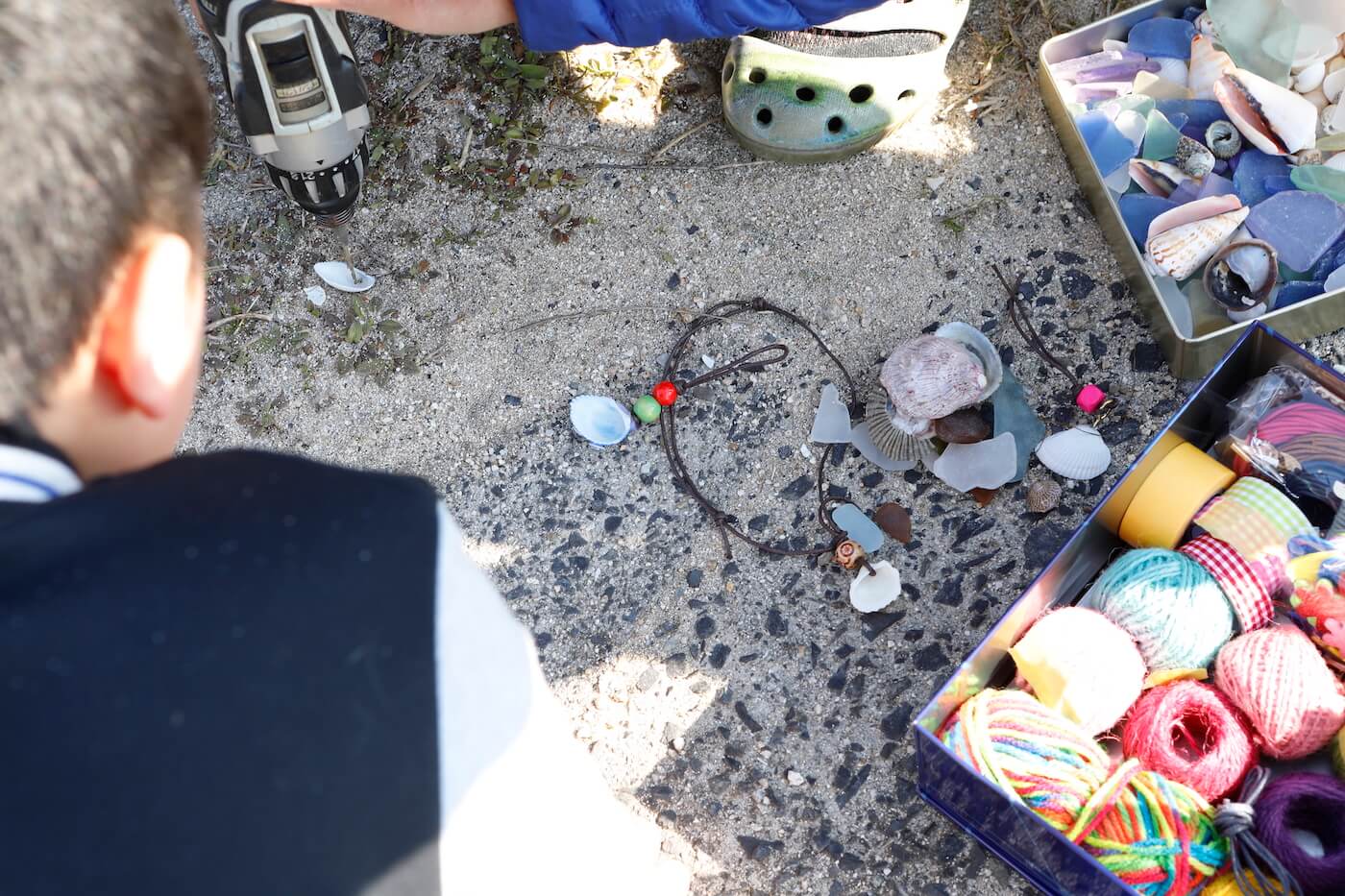 写真:砂浜の上に並ぶシーグラスやアクセサリーのパーツを選ぶ子ども