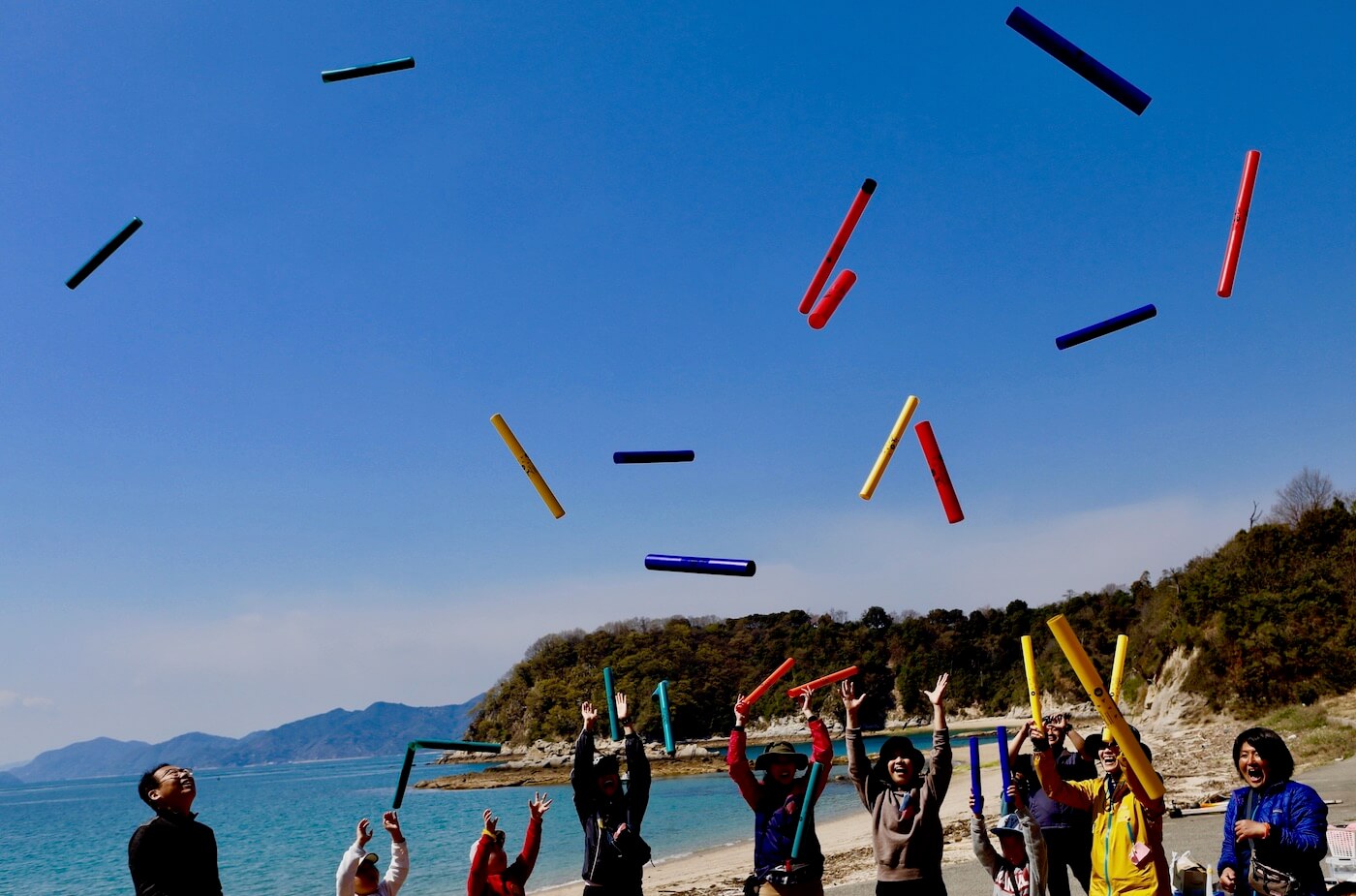 写真:カラフルな棒でできた楽器を空に放り投げる複数の子どもや大人