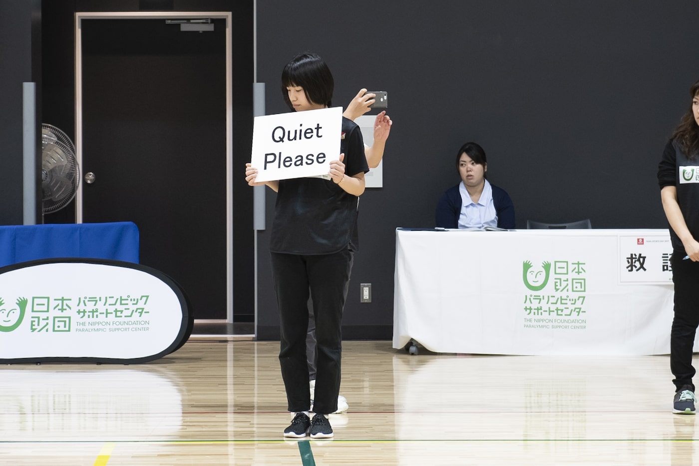 写真:「Quiet Please(静かにしてください)」という札を持つ女性