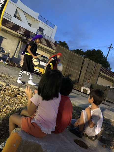 写真:屋外を練り歩く太鼓の演奏を聴く子どもたち