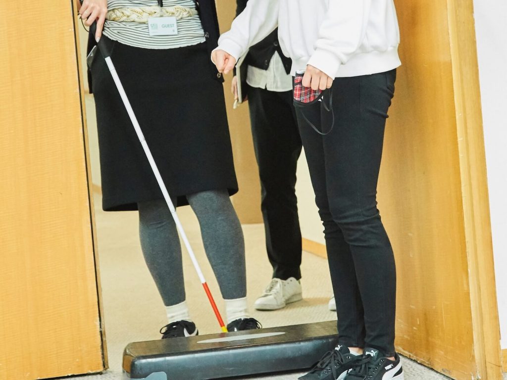 写真:白杖を使って段差を越えようとする女性をサポートする祝さん