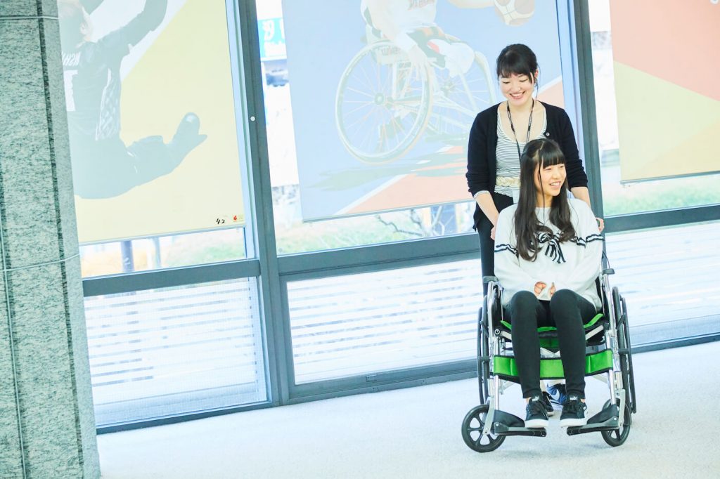 写真:車いすに座る祝さんと、車いすを押す女性