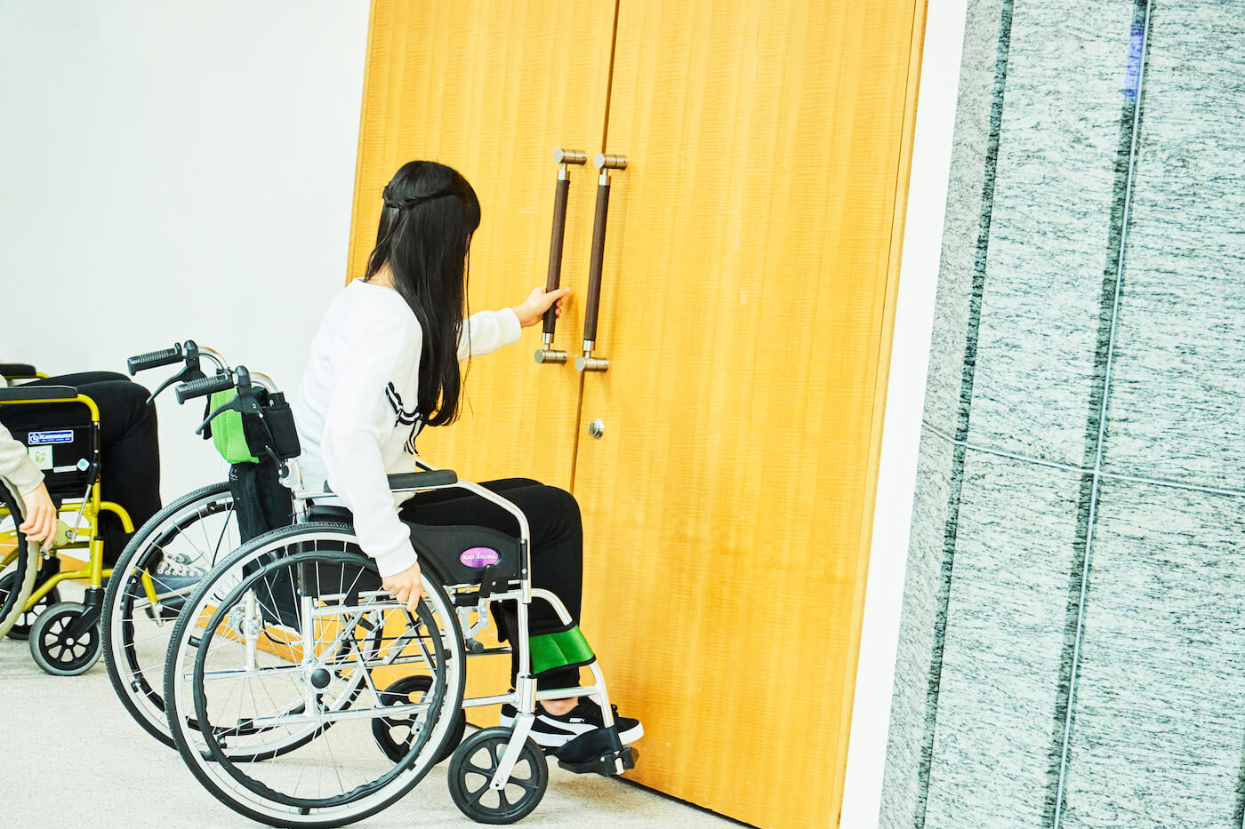 写真:車いすに座った状態で引き扉を開けようとする祝さん