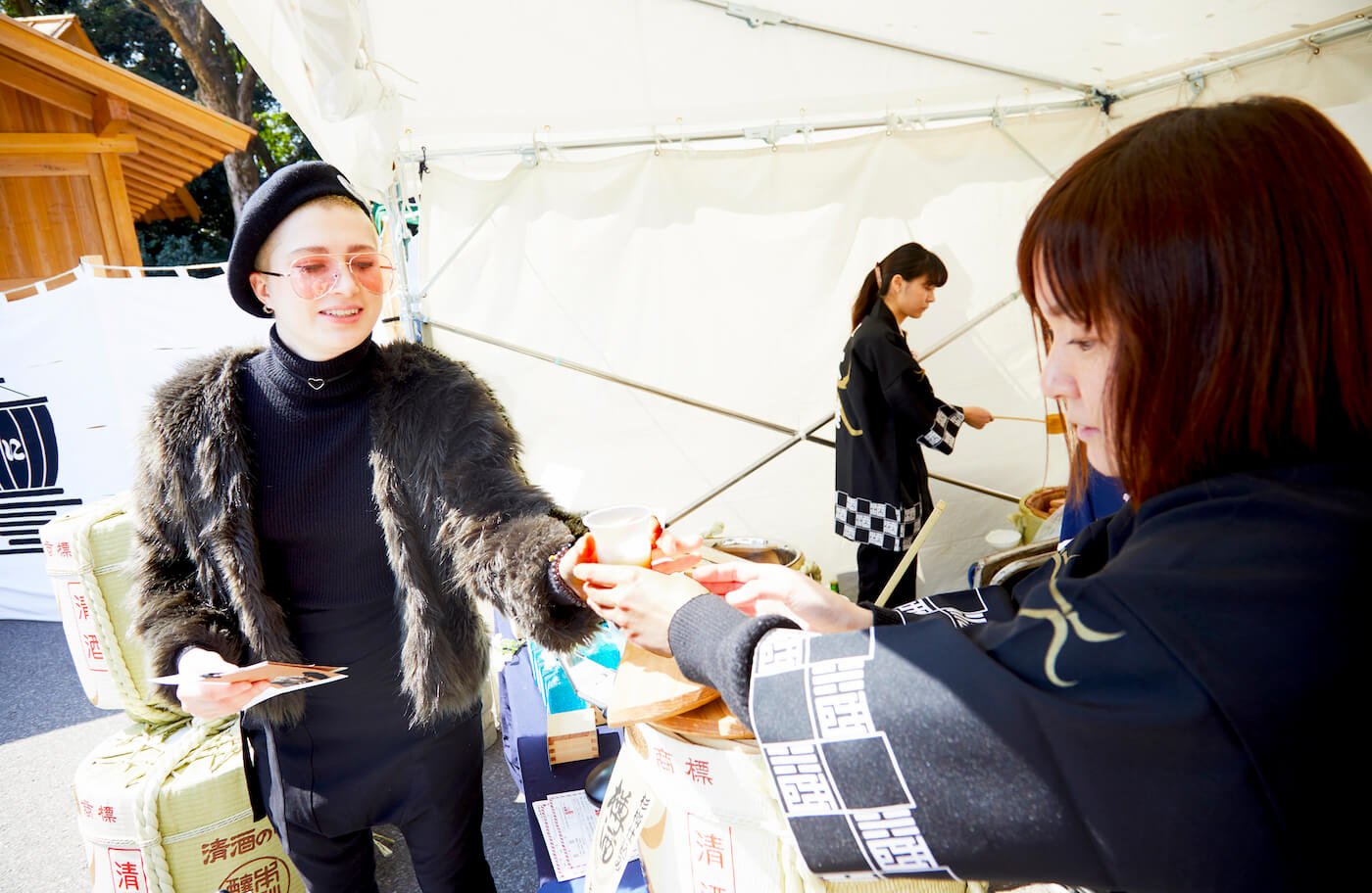 写真:売店スタッフから甘酒を受け取るナナさん(左端)