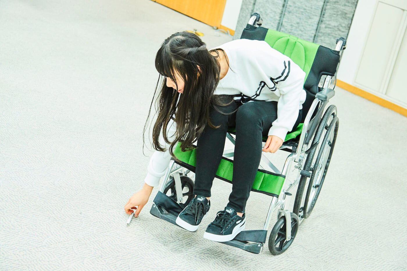 写真:車いすに座った状態で床に落ちたペンを拾う祝さん