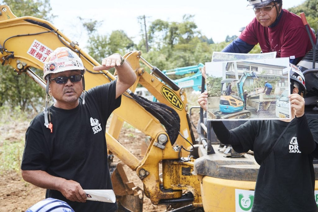 写真:家の前の道路に流れ着いた水上バイクを小型重機で撤去する作業を、写真を見せながら説明する黒澤さん。