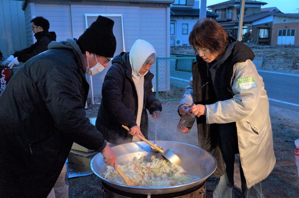 写真:毎週金曜日、金山保育園の前で開かれている炊き出しの様子。支援団体のメンバーら3人が、野菜が入った大きな鍋を囲んでいます