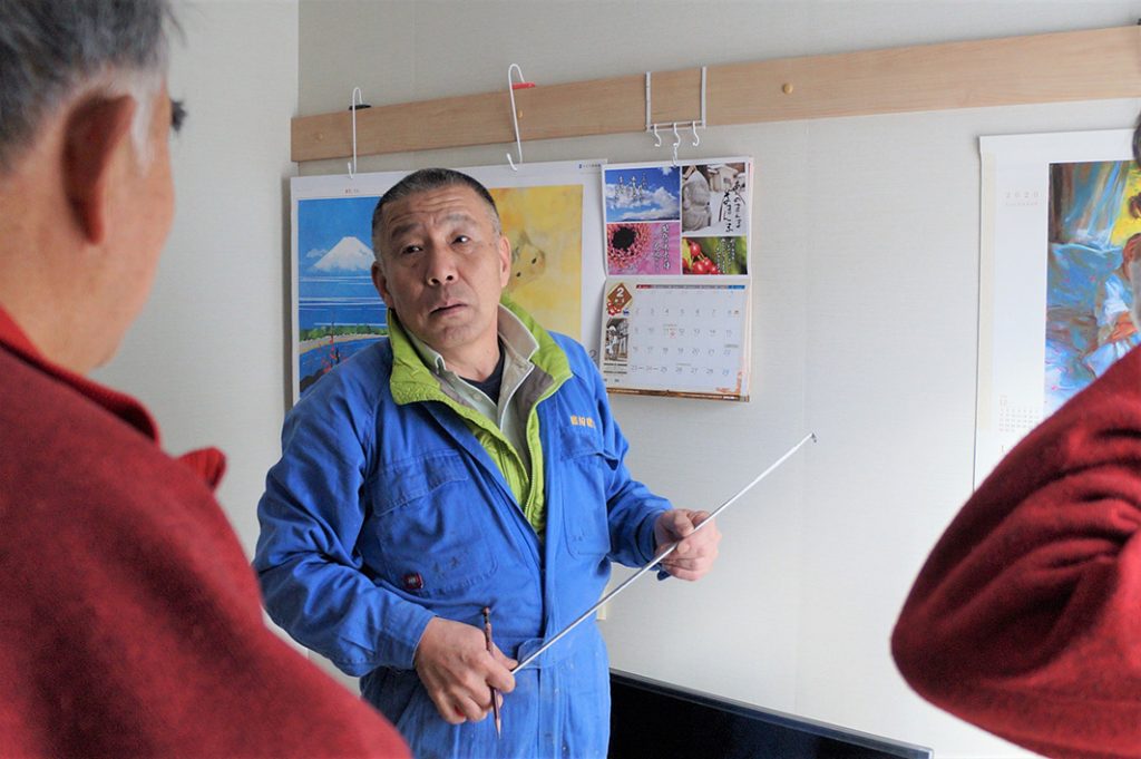 写真:住民の要望を聞き取る渡辺功さん。青い作業服姿で、メジャーを手に話をしています