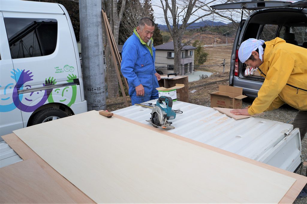 写真:外に設けた仮設作業台の上で、木の板を裁断し、やすりをかける功さんら