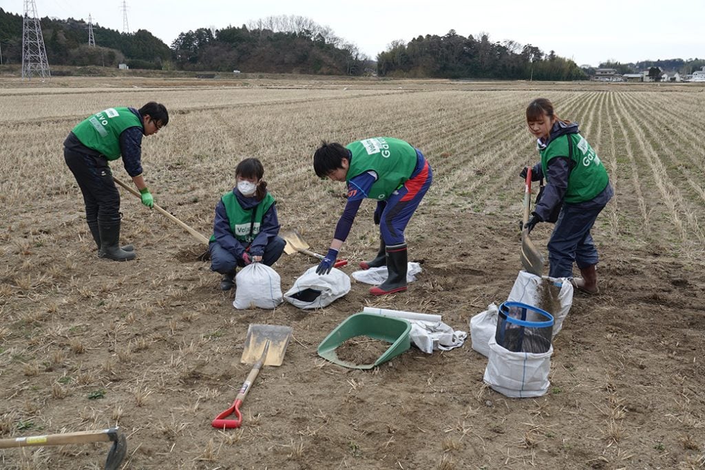 写真:田んぼからスコップを使って表面に広がった石などを取り除く学生ボランティア