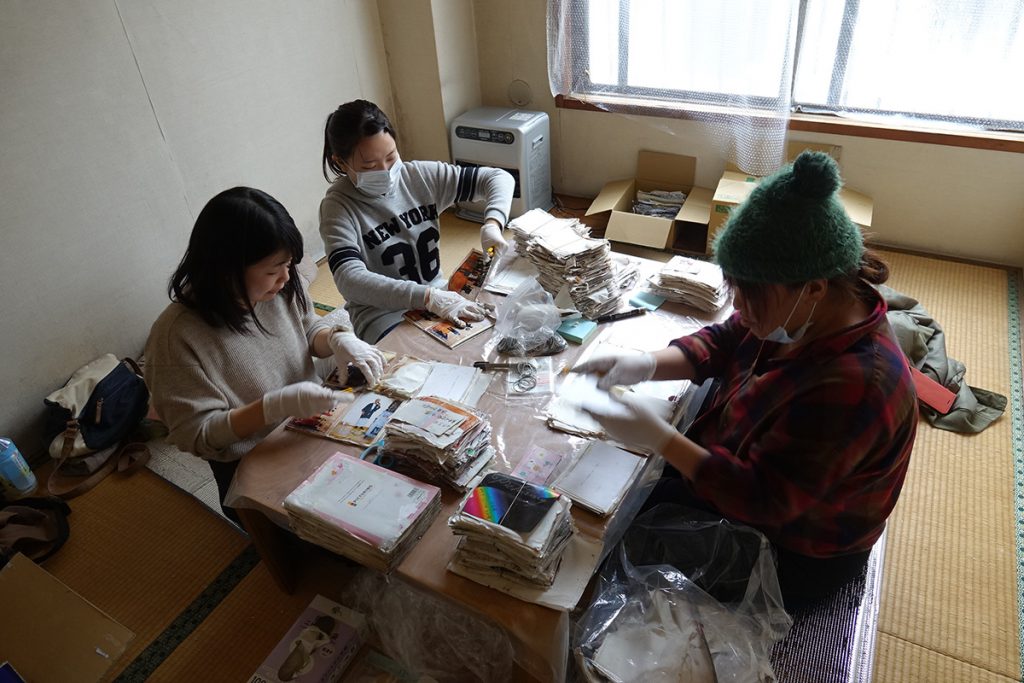 写真:テーブルの上に、水に浸かったアルバムを並べて、写真を切り出す3人のボランティア