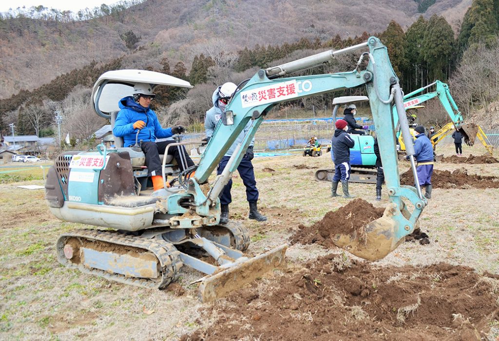 写真:小型ショベルに乗って、扱い方の講習を参加者が受ける様子