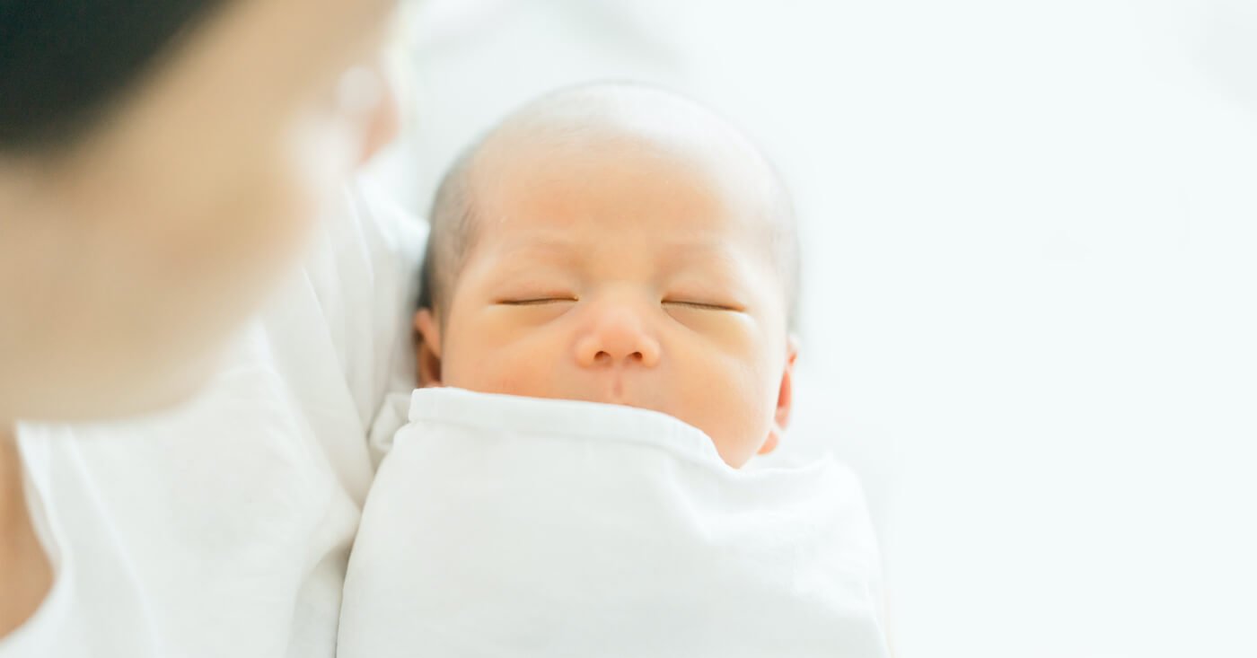 写真:眠る赤ちゃんを抱く妊婦