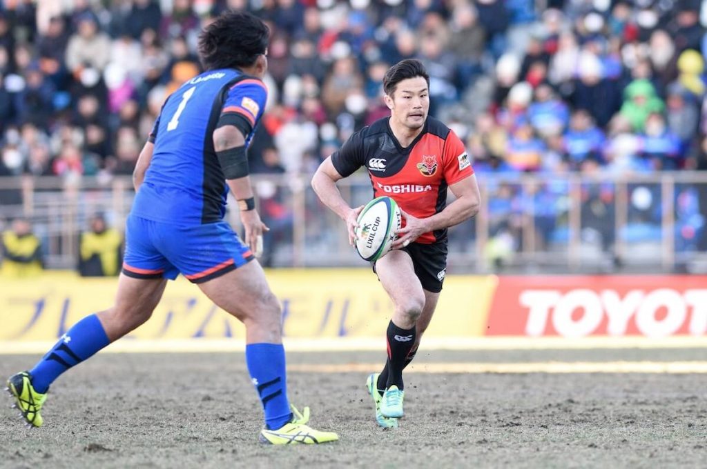 写真:フィールド上をラグビーボールを持って走る廣瀬さん(右)と阻止しようとする対戦チームの選手