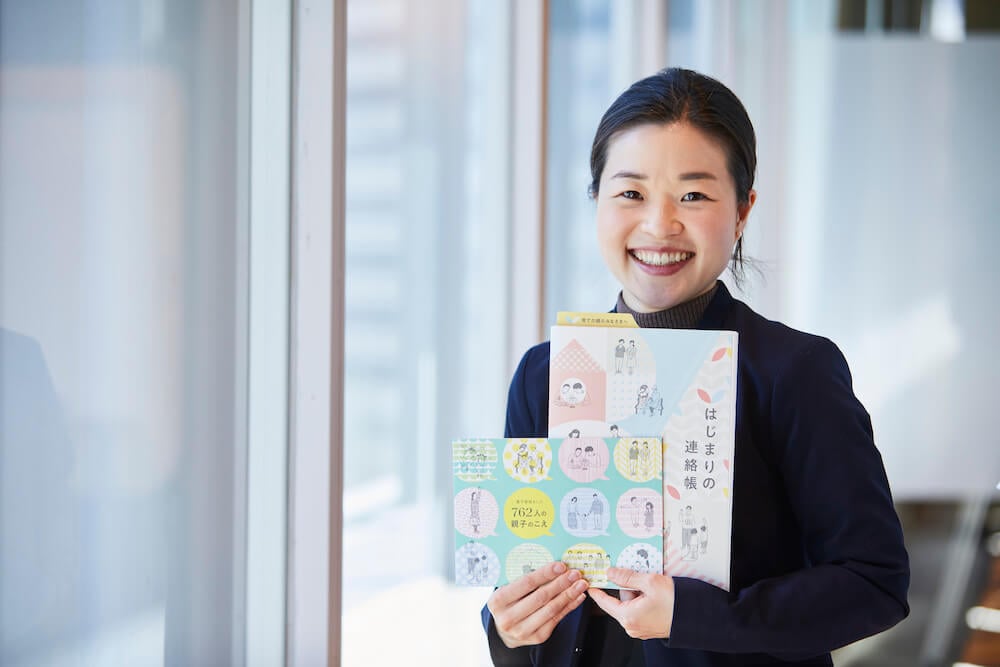 写真:日本財団が作成した冊子「はじまりの連絡帳」「養子縁組をした762人の声」を手に持ち微笑む新田さん