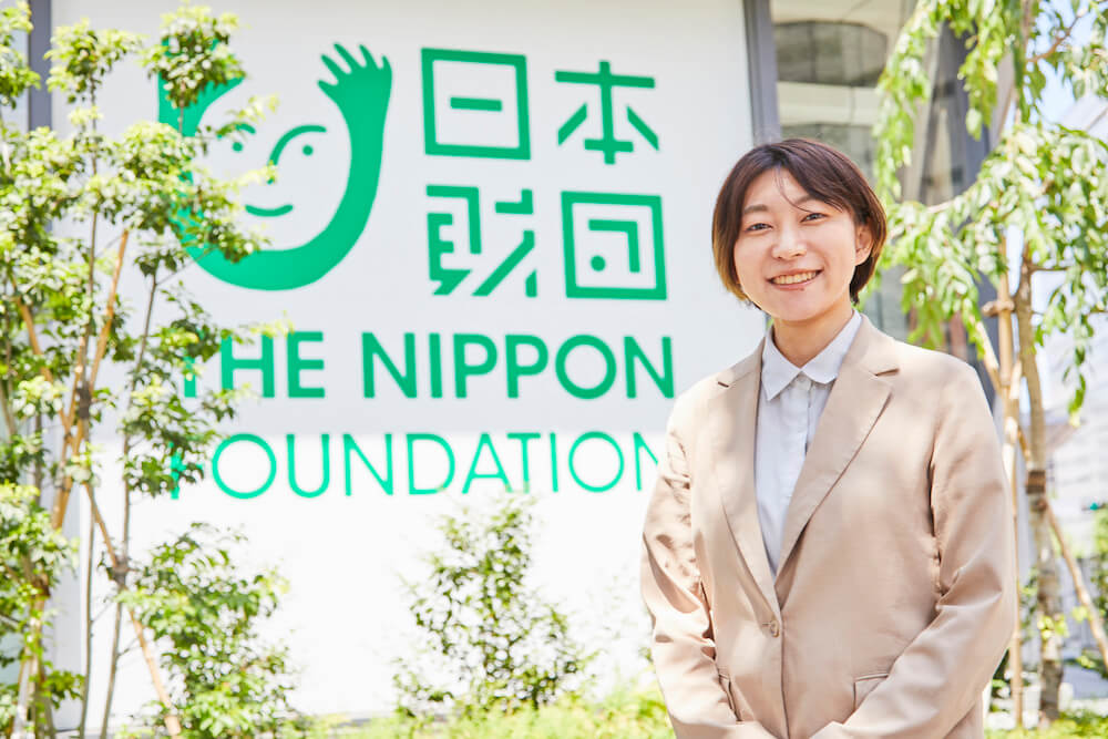 写真:日本財団のビルの前で笑顔を向ける長谷川さん