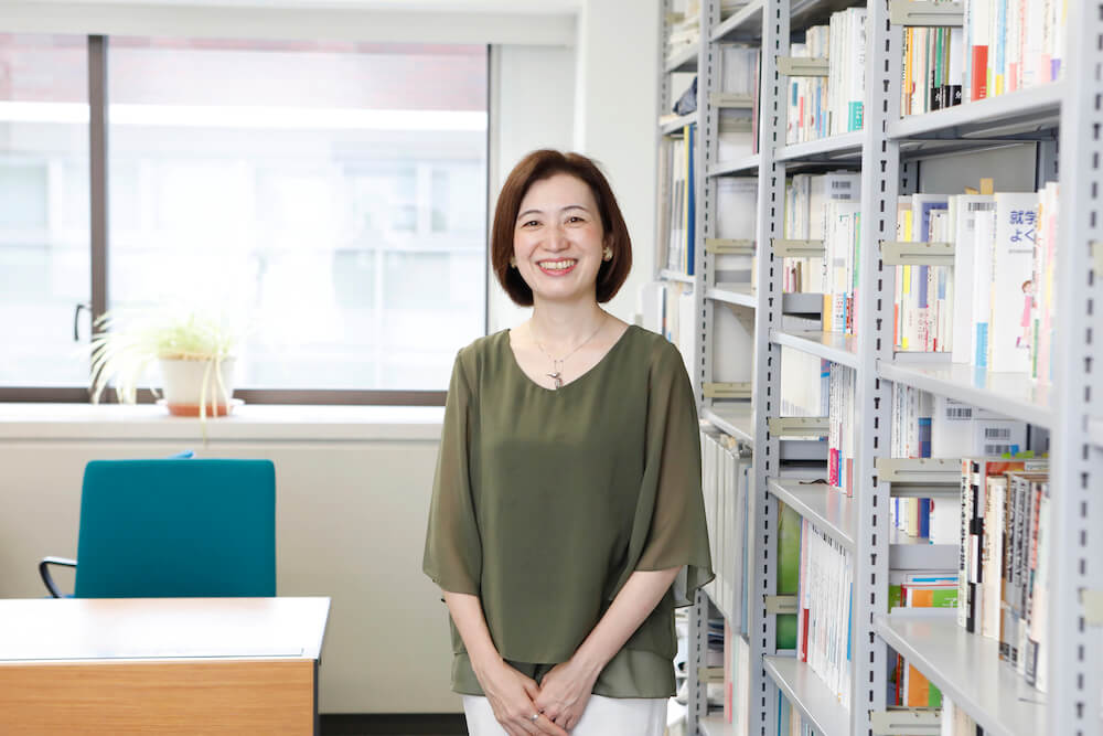 写真：大学の自身の研究室にて、たくさんの書籍をバックに笑顔を向ける澁谷さん