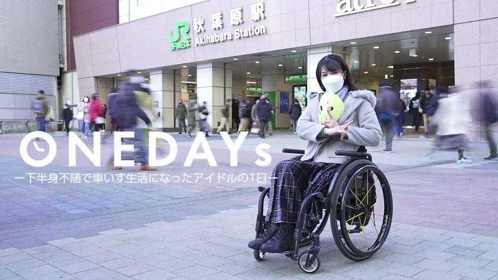 画像：駅の前で決めポーズをとり笑顔を向ける車いすに乗った猪狩ともかさん