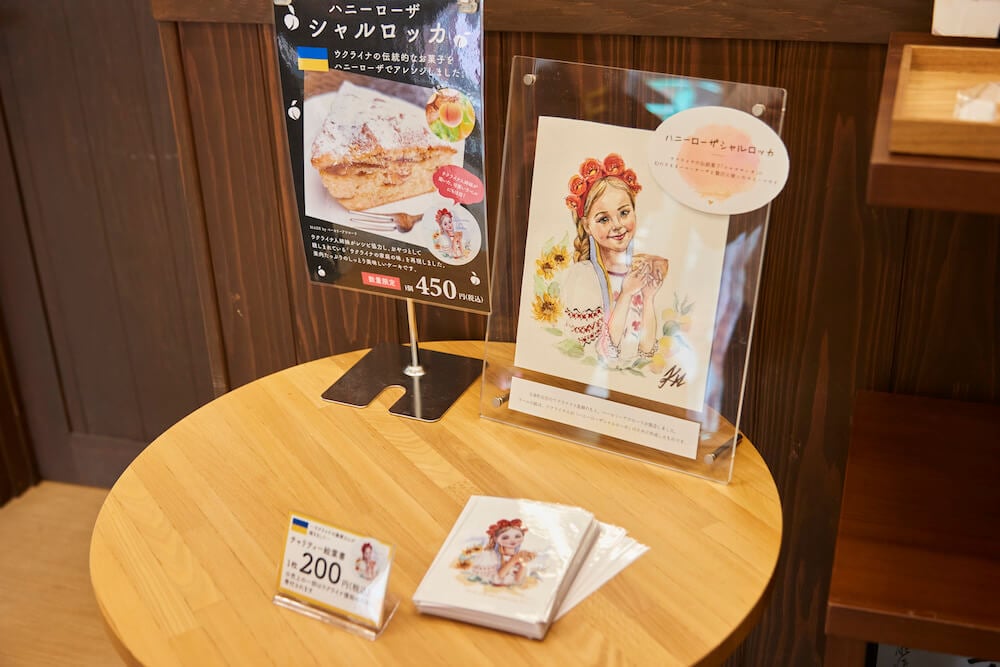 写真:観光拠点施設のテーブルに飾られた限定スイーツのポップ(左)と、ウクライナ避難民が描いた少女のポストカード(右と手前)