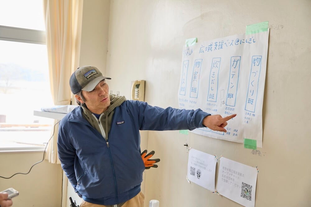 写真:壁に貼られた、役割ごとに区切られた「班」について、指を指しながら説明する吉村さん