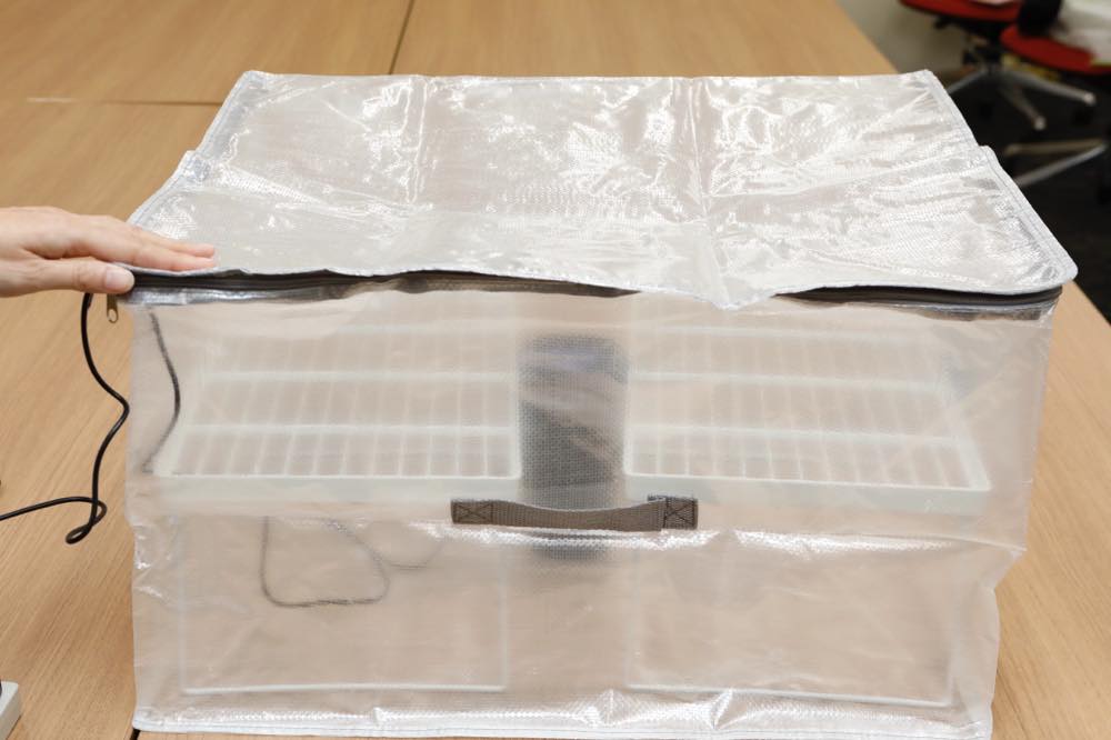 ファスナー付きの透明な折りたたみ収納ケースの中に、車載用ナノイー発生器と折りたたみ式の積み重ね棚が2個入っている。これが「なんでもバッグ」