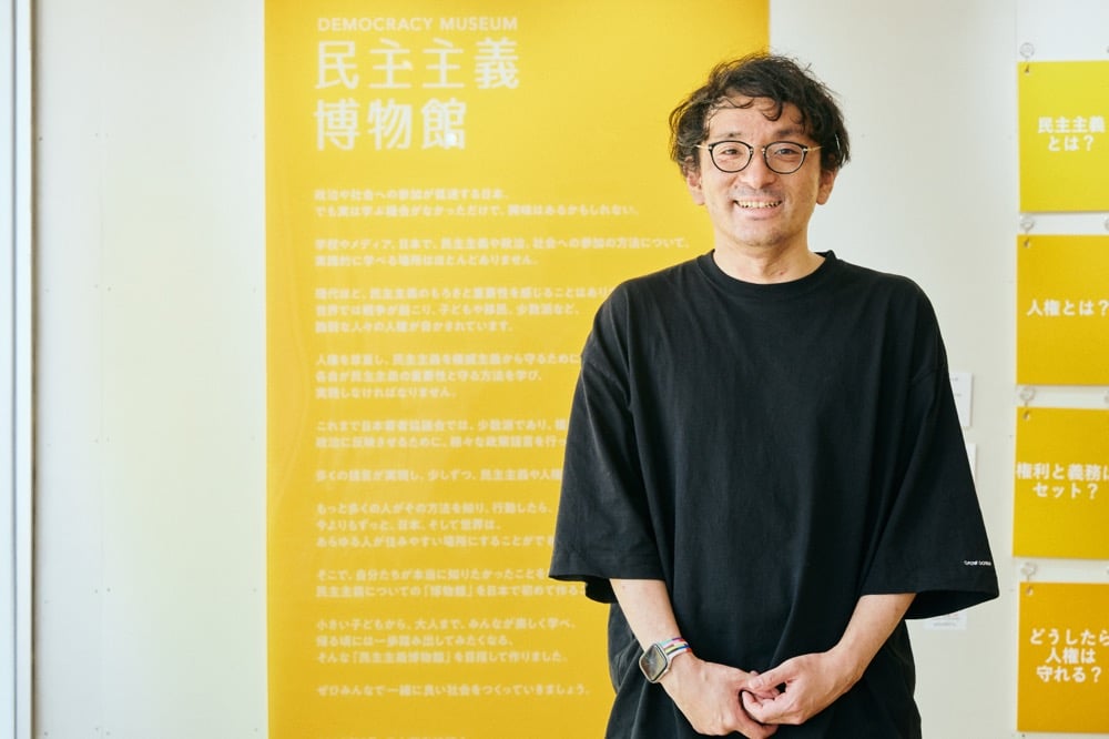 民主主義博物館の看板の前に立つ室橋さん