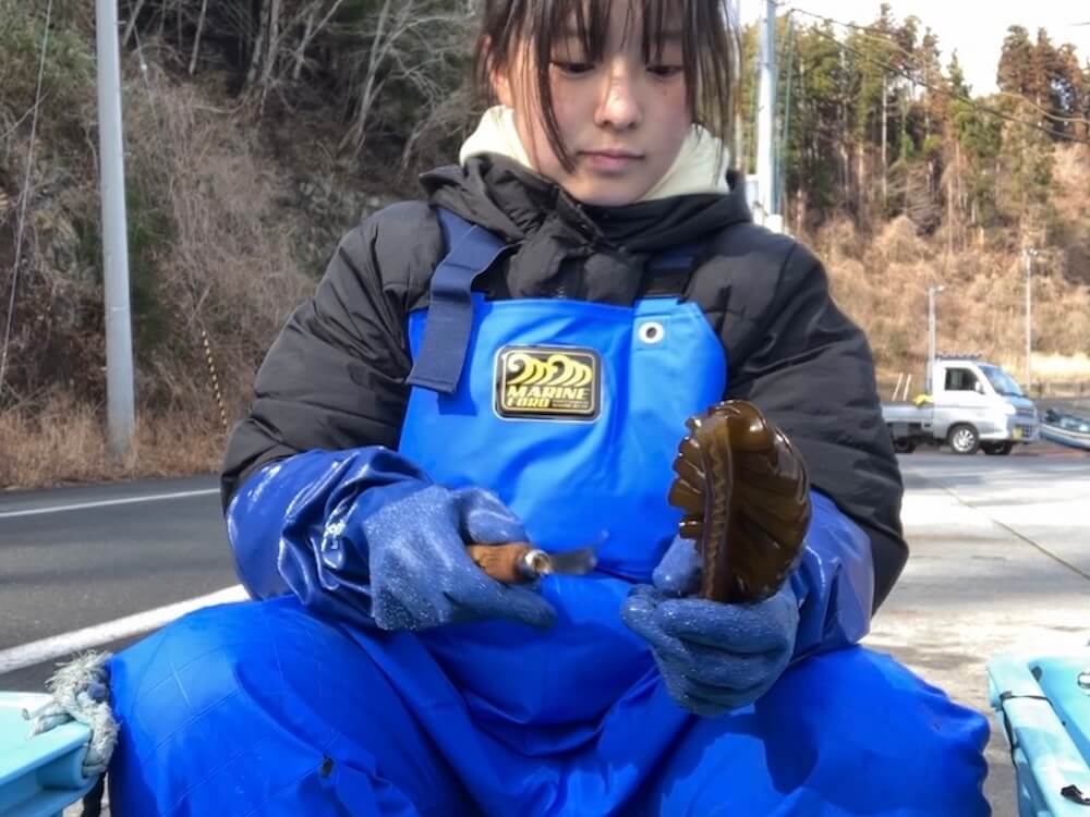 漁業用のエプロンを着てワカメを洗う大沼七奈さん