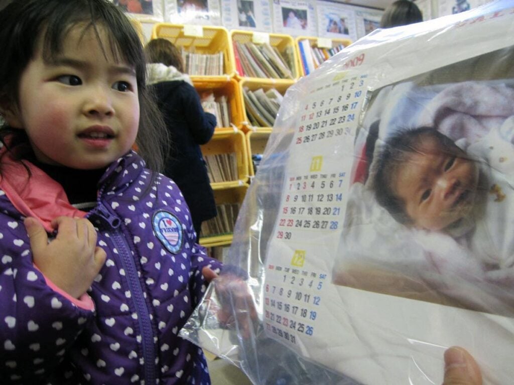 小さな女の子が、ビニール保護された自身が乳児だった時の写真を見つめている